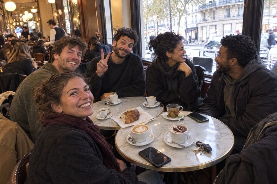 Un groupe autour de cafés dans une brasserie parisienne, un garçon fait le signe peace face à l'objectif